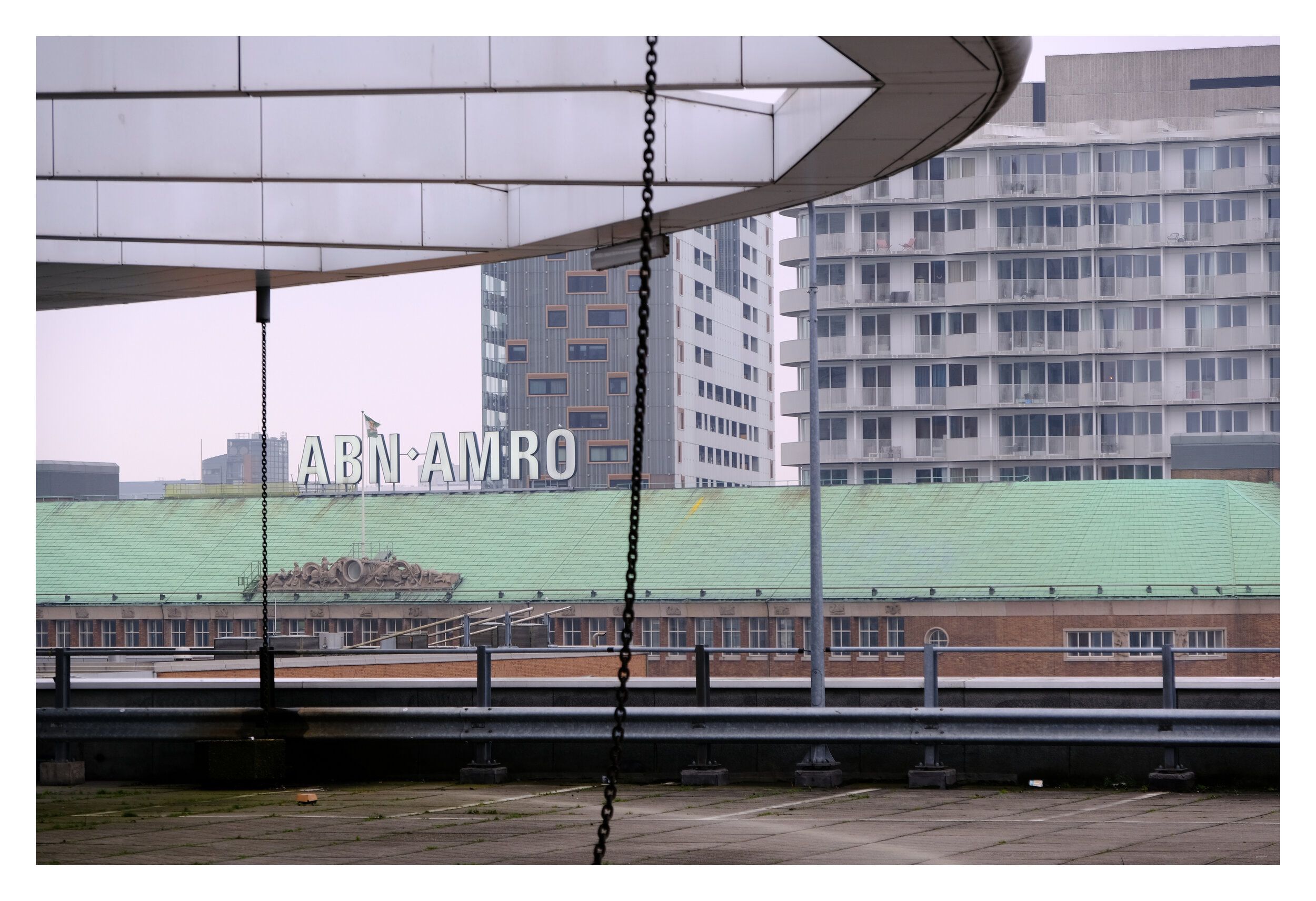 A curved concrete canopy framing an office building with the ABN AMRO sign, flats behind.