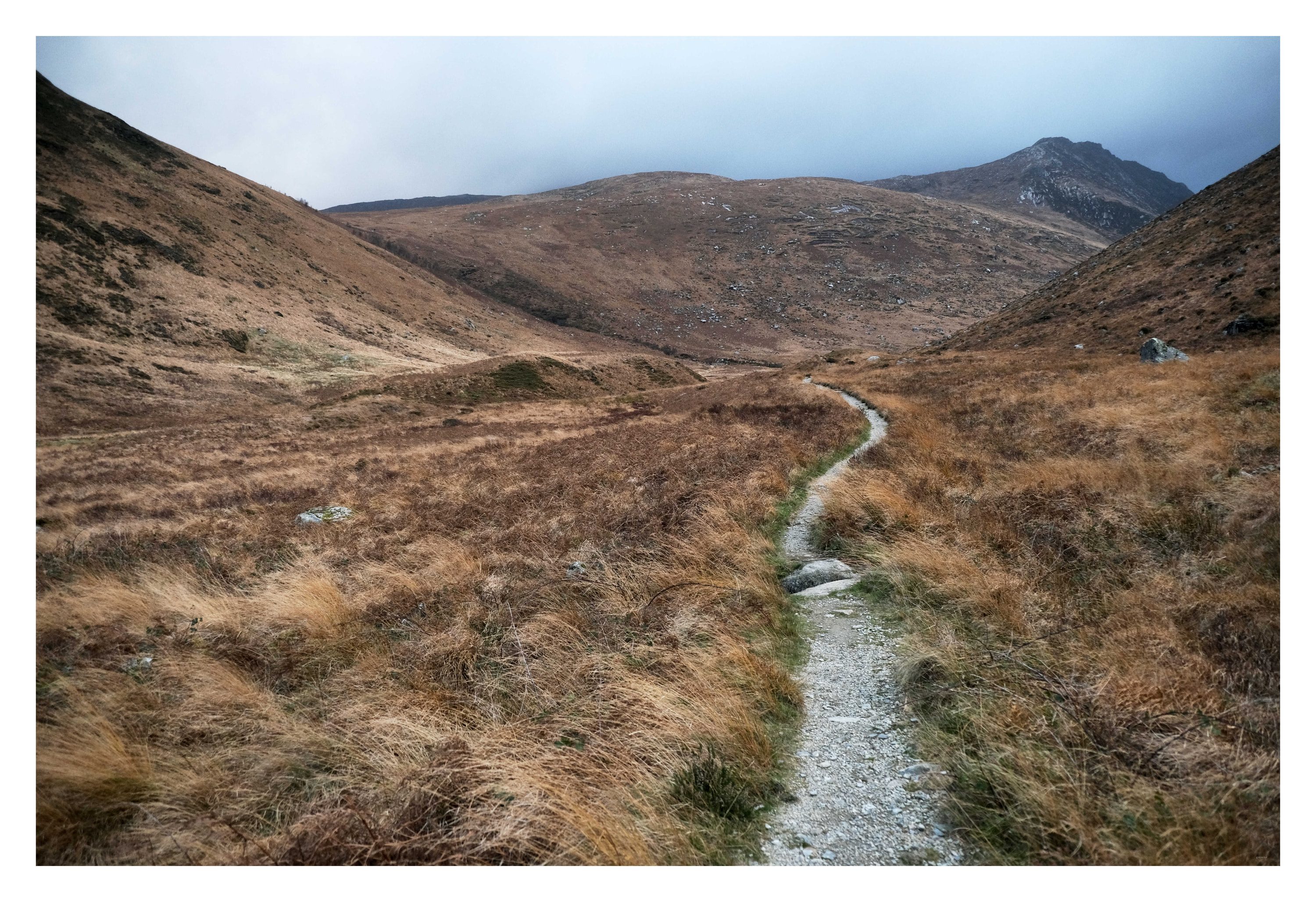 A narrow gravel path winding up a brown moorland glen towards bare mountains under a pale sky.