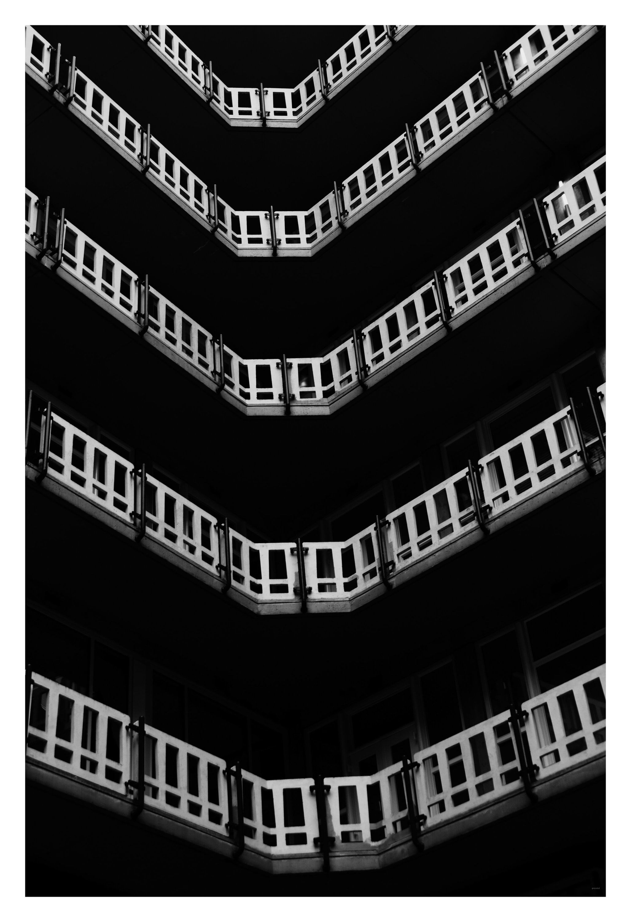 Black-and-white view up a building's stacked balconies, forming repeating chevrons.