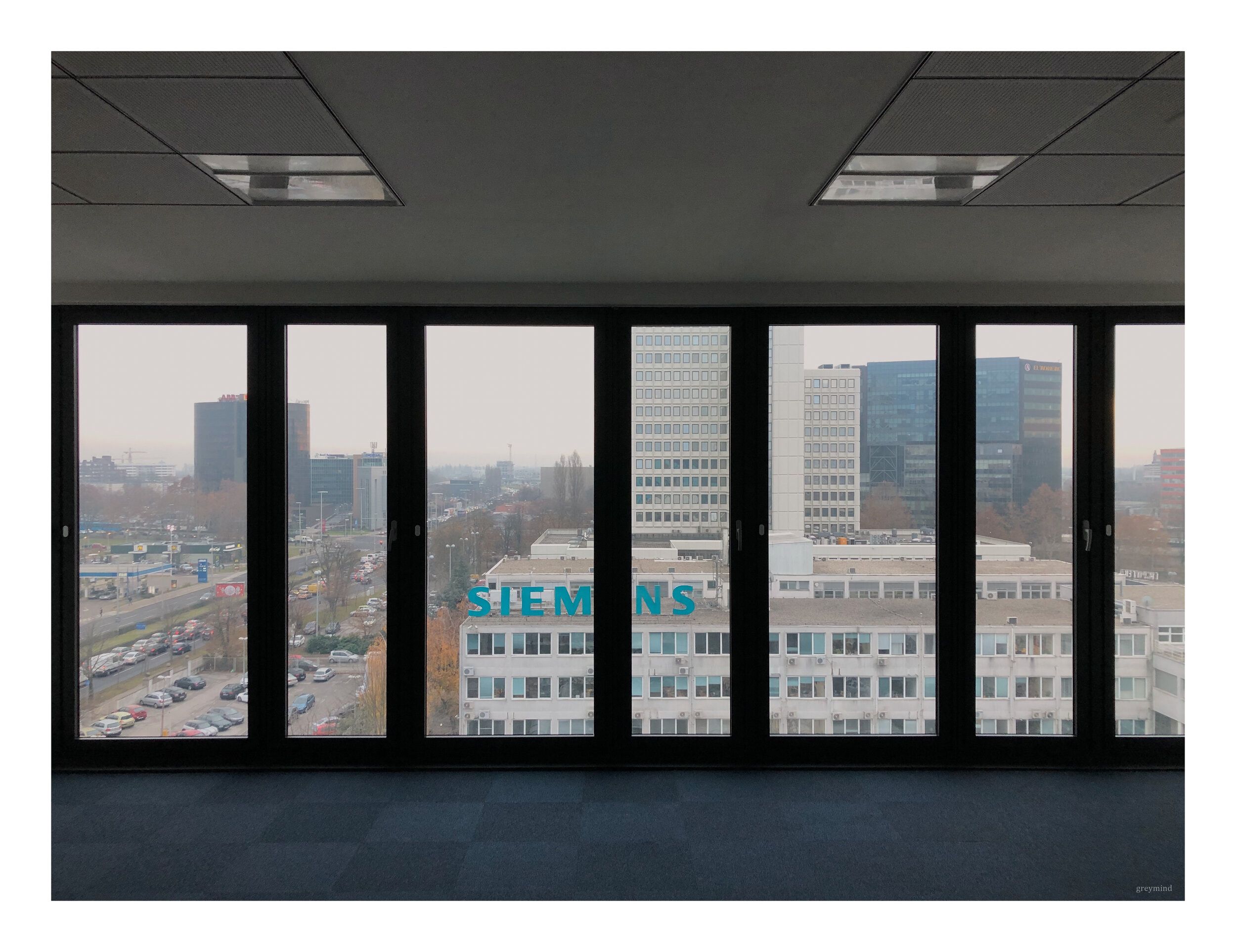 Floor-to-ceiling office windows looking out over city towers, one bearing the Siemens sign.